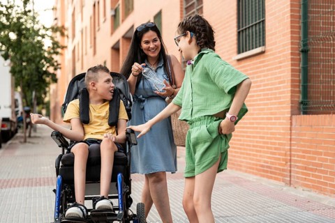A family shares a joyful moment outdoors with a girl with a tracheostomy and a boy with cerebral