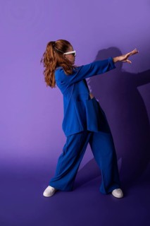 A young woman dancer in a stylish blue outfit poses dynamically against a vibrant purple background