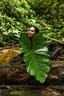 A young Ecuadorian woman with eyes closed, partially covered by a large leaf, is surrounded by the