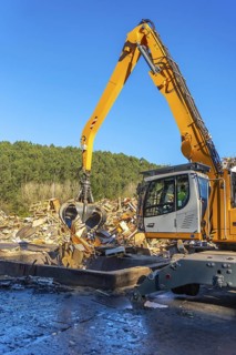 Vertical photo of an excavator moving waste outside a recycling plant