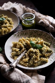 A rustic bowl of spiral pasta tossed in vibrant green pesto sauce, adorned with fresh basil. An