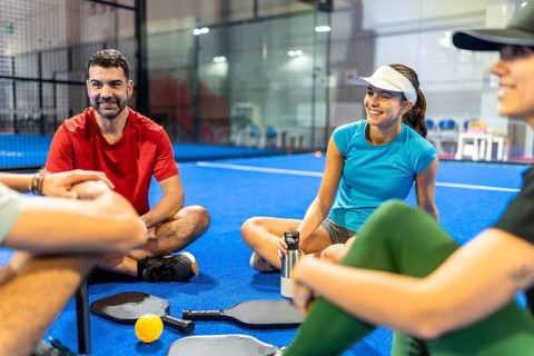 Group of young friends enjoying a break, sitting and smiling on the blue pickleball court with