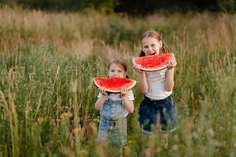 Two children enjoying juicy watermelon slices while standing in a lush green field during summer.