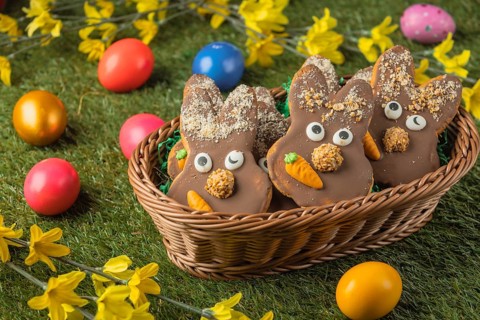Bunny shaped Easter cookies with chocolate and carrot in a basket surrounded by colorful eggs on