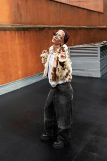 Fashionable woman in stylish faux fur jacket and sunglasses poses confidently against an urban