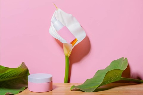 A delicate pink cosmetic jar placed beside a vibrant calla lily flower against a soft pink