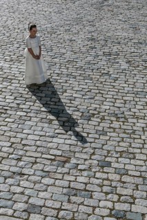 A young girl stands gracefully in a traditional First Communion dress on a cobblestone path,