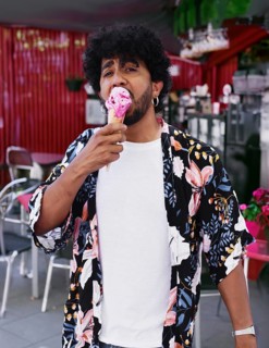 A man in a vibrant floral shirt enjoys a delicious ice cream cone during a sunny summer day. He