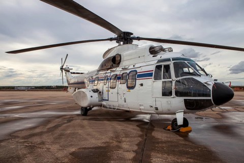 A white military helicopter with blue and red stripes is parked on the wet tarmac at an air base.