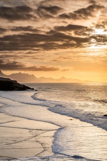 Gentle ocean waves wash onto the shore of La Pared Beach in Fuerteventura at sunset. The golden