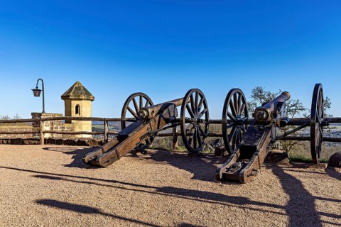 Two old cannons on a sunny spot with a clear sky and a railing in the background, The cannons on