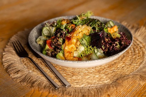 A vibrant green salad topped with crispy king prawns in batter, served in a ceramic bowl on a