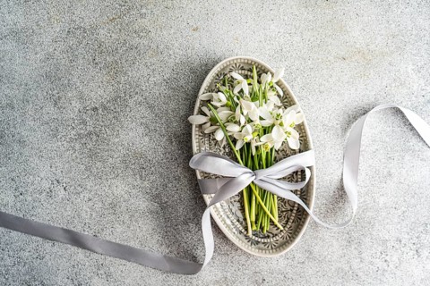Top view of delicate spring snowdrops tied with a silver ribbon in an ornate vintage plate on a