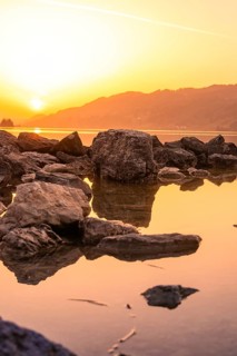 Rocks in calm water at sunset, outlines reflecting in clear lake, Großer Alpsee, Immenstadt im