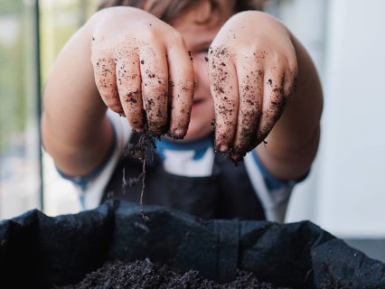 Cropped unrecognizable child busily engages in gardening, their hands covered in dirt, symbolizing