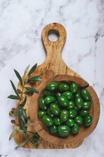 Halkidiki olives, classic Greek green olives, in a wooden bowl, on a cutting board, top view,