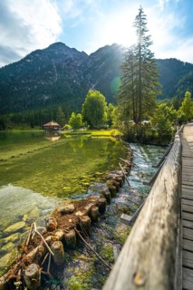 Crystal clear water flowing under a wooden bridge in lake dobbiaco, surrounded by majestic