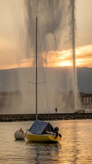 A serene scene captures a sailboat on Lake Geneva during a beautiful sunset, with the iconic Jet