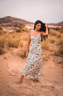 Portrait of a Caucasian brunette stroking her hair in a white floral dress, in the sand on the