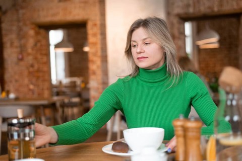A woman in a green sweater enjoys her morning at a cafe. The table setting includes breakfast items