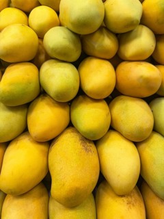 A vibrant display of fresh, ripe mangoes piled closely together, showcasing their vivid yellow