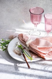 A tasteful arrangement on a shadow-dappled table featuring pink glassware, delicate snowdrops on a