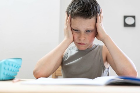 A young student intently reading a book, resting his head on his hands, illustrating focus and