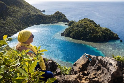 A female tourist enjoys the stunning view of the blue waters and lush islands of Raja Ampat,