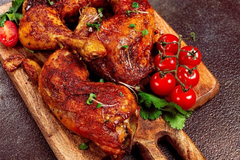 Grilled fried chicken legs, served with fresh cherry tomatoes, and herbs, on a wooden chopping