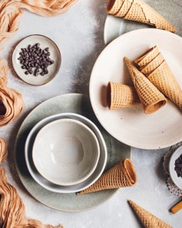 A flat lay of empty waffle cones, ceramic bowls, and a small dish of chocolate chips arranged on a