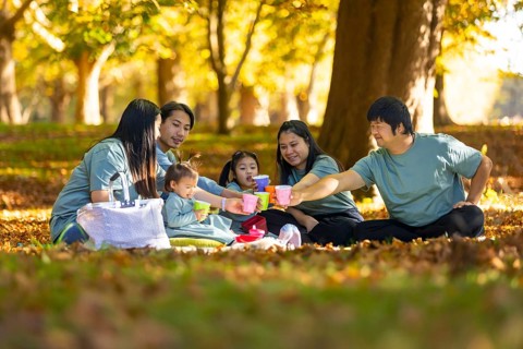 Asian family shares joyful moments at a park picnic amidst autumn leaves. Parents and children