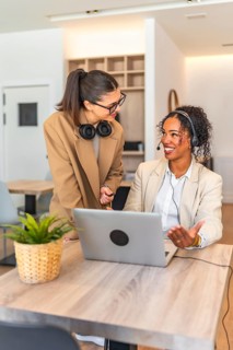 Two businesswomen collaborating on a laptop, showcasing teamwork and communication in a
