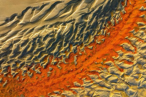 A mesmerizing aerial view of sand dunes with striking orange and beige hues, showcasing the beauty