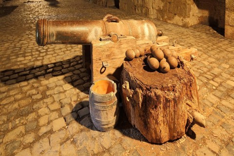 Medieval cannon with ammunition and cannonballs, powder keg, historic gun, underground, interior