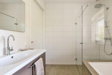 A contemporary bathroom featuring white tiled walls, a glass shower door, and sleek silver fixtures
