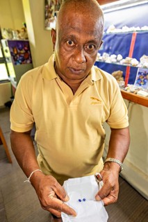 Elderly man wearing a yellow shirt shows two precious stones in an exhibition, The Sapphire