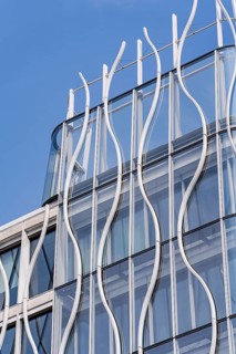 A modern building facade showcasing flowing metal and glass elements against a clear blue sky. The