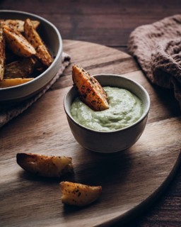 A rustic presentation of seasoned potato wedges served with creamy dip on a wooden board. Perfect