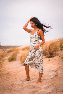 Portrait of a Caucasian brunette stroking her hair in a white floral dress, in the sand on the