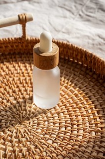 A frosted cosmetic with a wooden cap sits on a woven basket, bathed in warm sunlight, evoking a