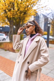 Vertical portrait of an african american model holding sunglasses wearing coat at city