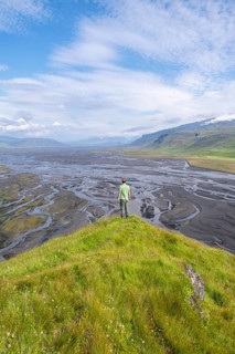 Hiker, young man on a hill, view over alluvial land, meandering river, Dímonarhellir, Suðurland,