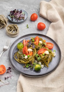 Tagliatelle green spinach pasta with tomato, pea and microgreen sprouts on a gray concrete