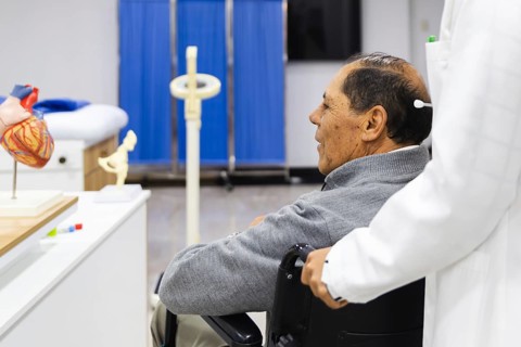 An elderly patient sits in a wheelchair while being cared for by a healthcare professional in a