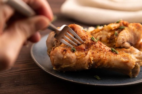 Fried Turkey Wing with spices and thyme on plate with hand on brown wooden background and linen