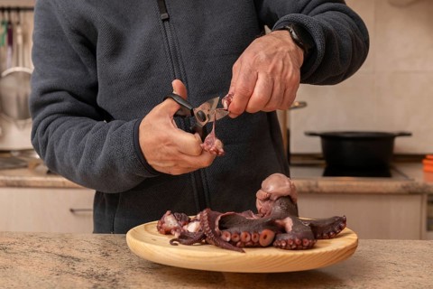 A man skillfully prepares fresh octopus on a wooden plate in a kitchen setting. This image captures