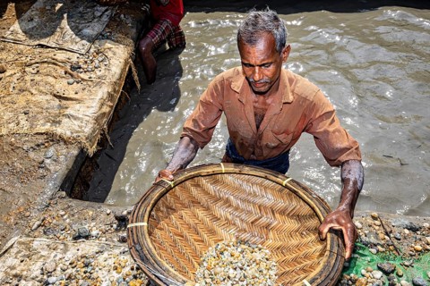 Man focuses on working in a pool of water with a filled basket, the sapphire and gemstone mines at