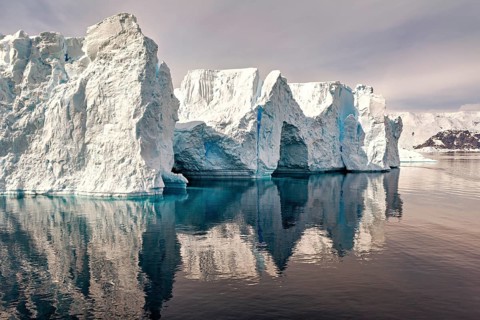 Massive iceberg with clear reflection in the water, against a blue sky, icebergs in the landscape