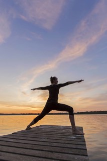 Woman practicing yoga posture Virabhadrasana II, Warrior Pose, lunging standing asana on jetty at