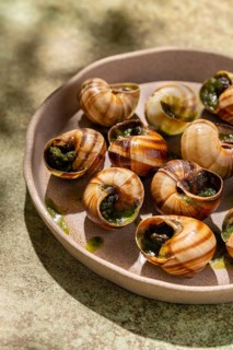 Baked escargots garnished with fresh parsley and drizzled with melted butter, served in a rustic